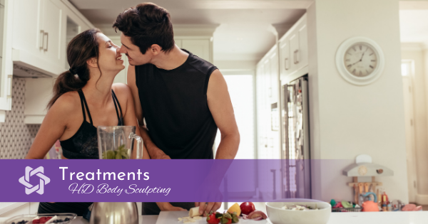 Young, healthy couple kissing in kitchen while making healthy smoothie