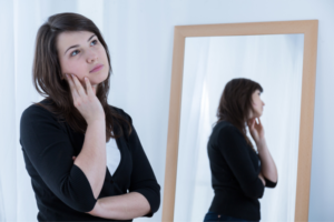 Young woman thinking with mirror at her side
