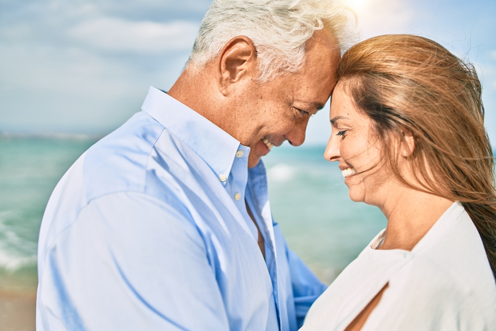 Couple smiling at each other on a beach, representing wellness and intimacy.