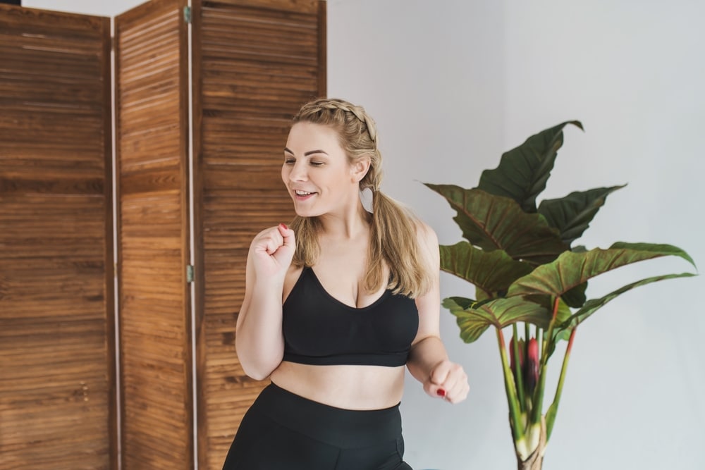 Woman exercising in a room with a wooden screen and plant.